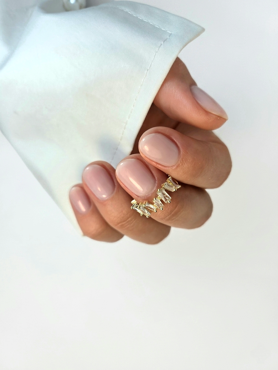 Korte nude nagels met een gouden ring, de hand komt uit een witte manchet